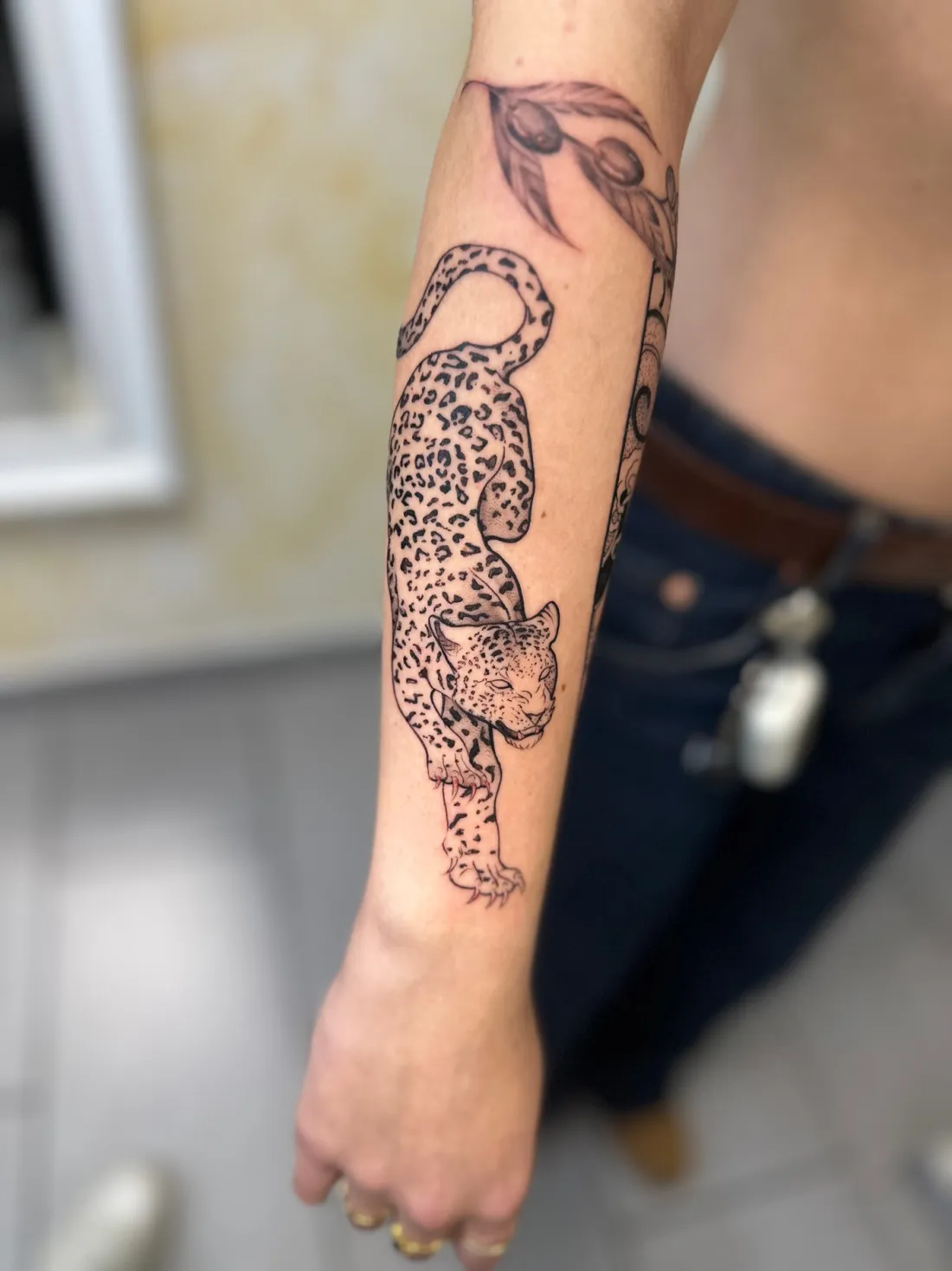 Kletternder Leopard mit Olivenzweig auf Unterarm — Fine Line Tattoo von Marko